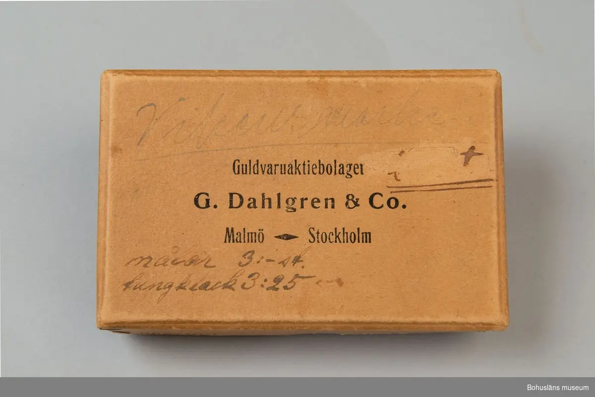 Brun papp. På locket texten: "Guldvaruaktiebolaget G. Dahlgren & Co Malmö Stockholm". 
Innehåller klubbmärken för Segelsällskapet Viken, Uddevalla;  UM23566:002 och UM23566:003.