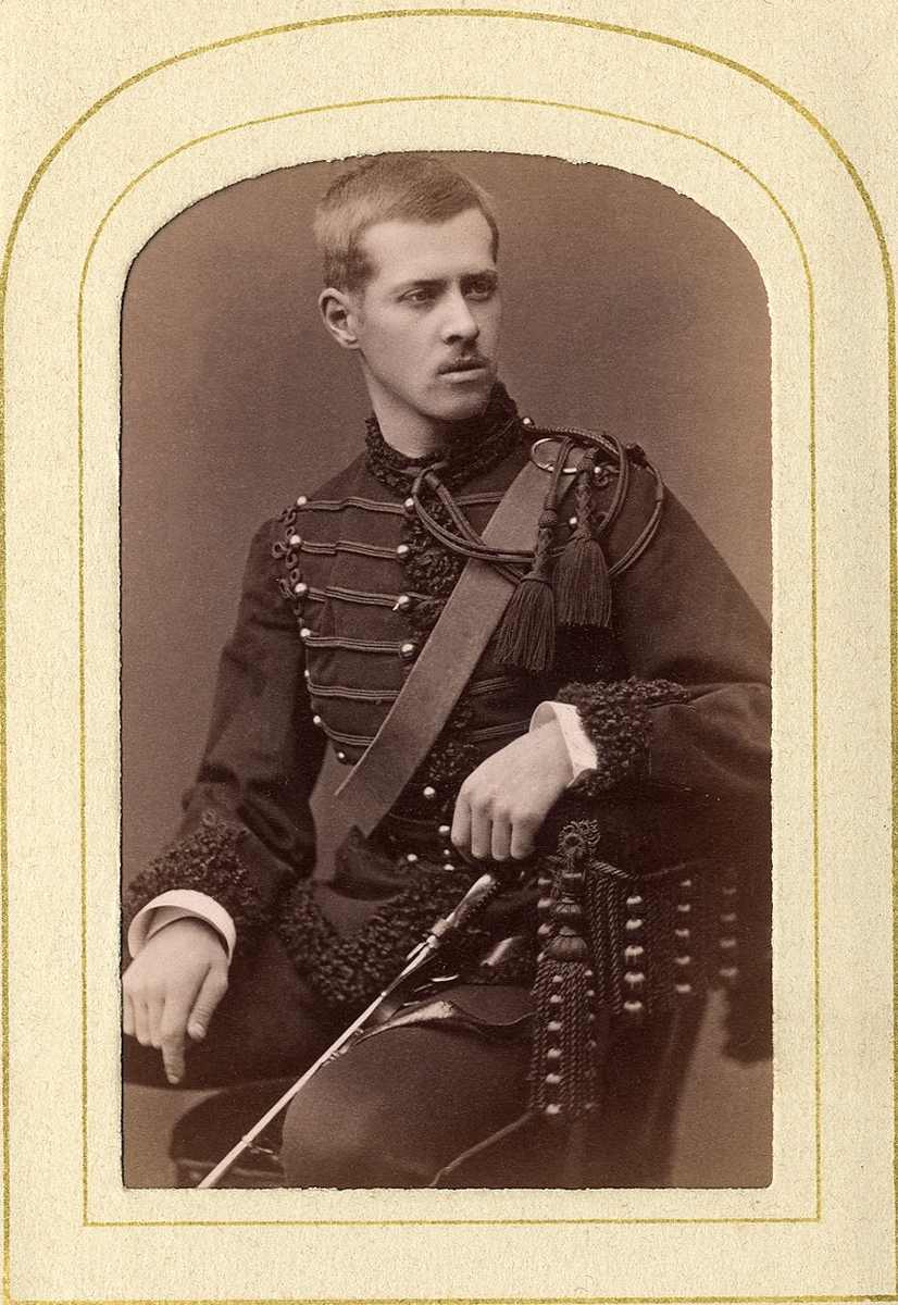 En man i militäruniform med fårskinnsgarnering. På baksidan av fotot står antecknat: "Schwerin". 
Knäbild, halvprofil. Ateljéfoto.