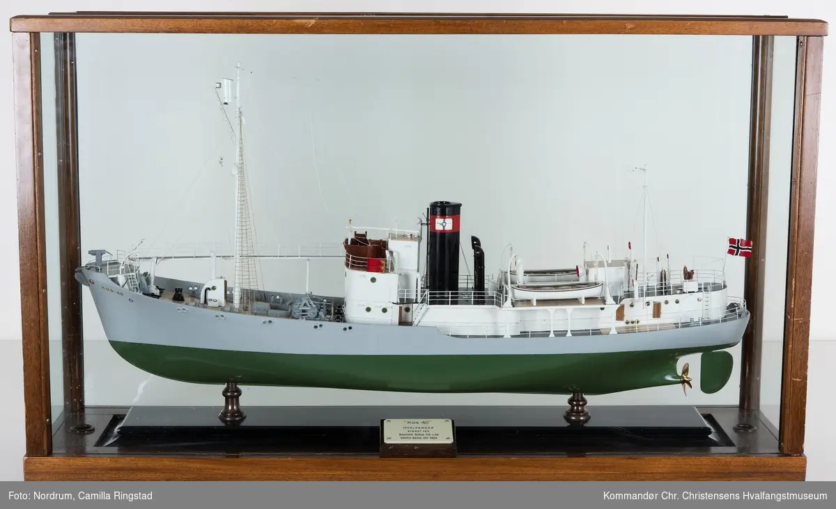 Miniatyrmodell av hvalbåten "Kos 40" tilhørende Hvalfangstselskapet Kosmos A/S i glassmonter. Skipet ble bygget ved Smiths Dock Co. Ltd. Middelsbrough, U. K. Modellen har tidligere tilhørt skipsreder Anders Jahre.