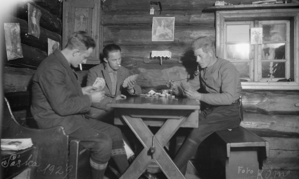Påsken 1929, tre menn som spiller kort i ei tømmerhytte. Bilder på veggen. Karl Olav Moe fremst.