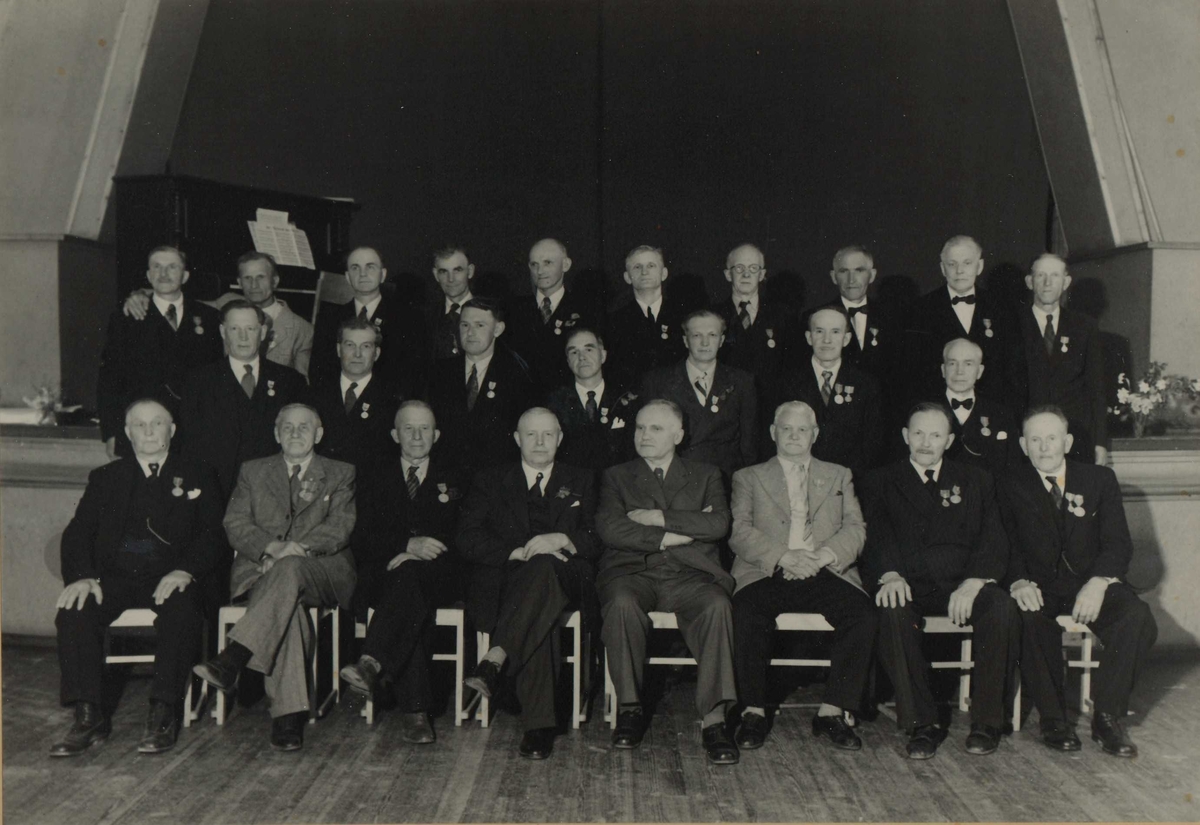 Gruppebilde av 25 menn hvor 23 er dekorert med Det Kongelige Selskap for Norges Vels Medalje for lang og tro tjeneste.  
