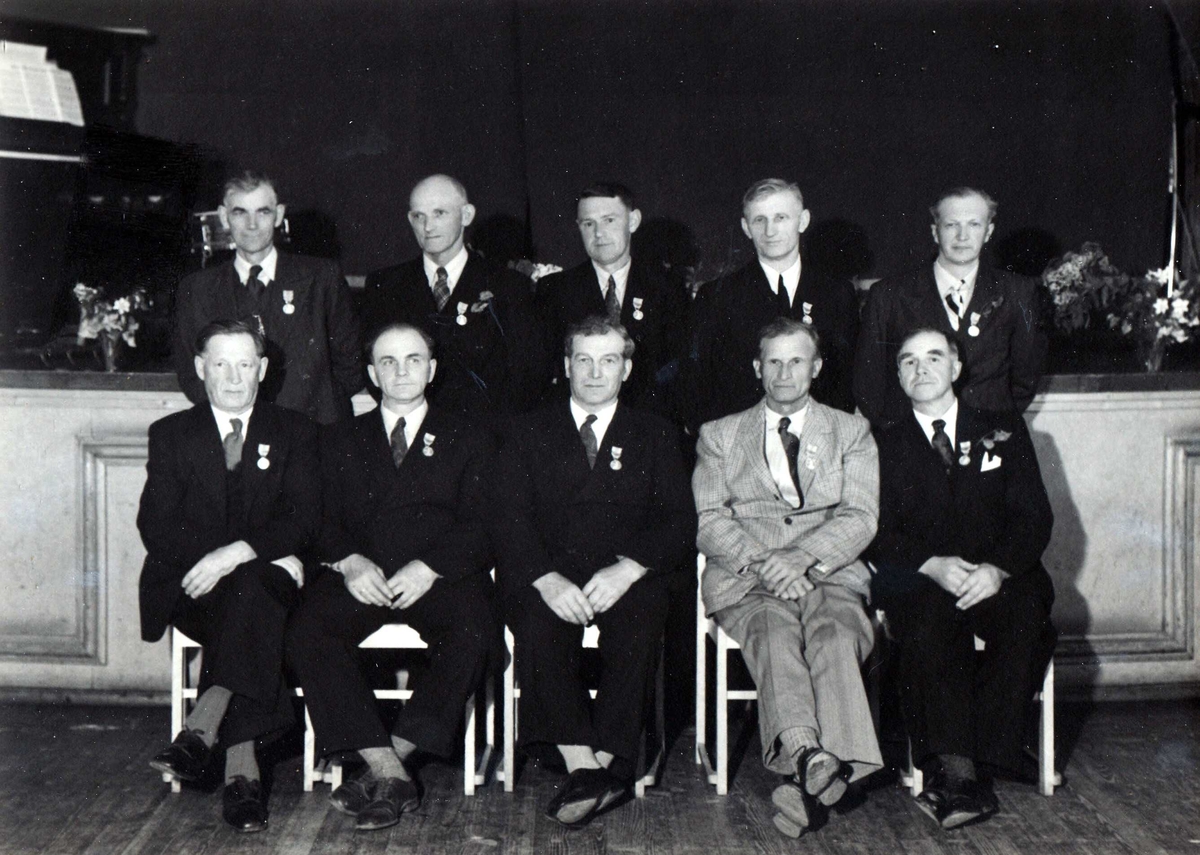 Gruppebilde av 10 menn dekorert med Det Kongelige Selskap for Norges Vels medalje for lang og tro tjeneste.