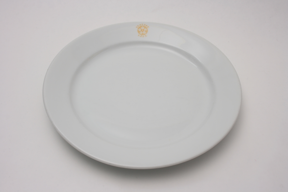 Flat, rund tallerken med skrå kant. På tallerkens kant finner man Trastad Gård emblem, Lutherrosen (blemst i sirkel med kors i midten) omgitt av ordene "Trastad Gård".