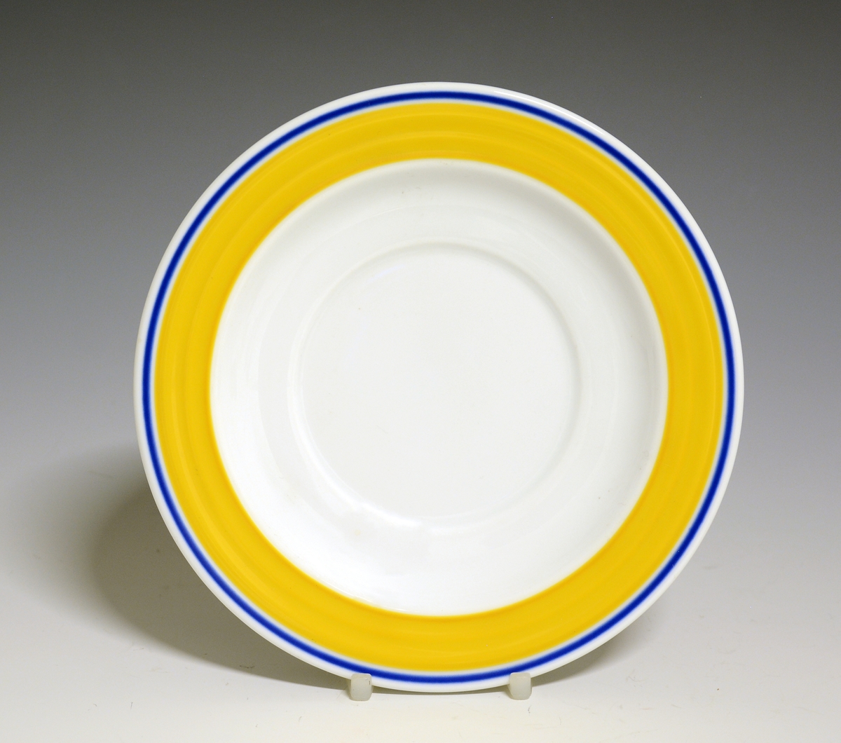 Teskål av porselen. Hvit glasur, fanen dekorer med et gult bånd og en blå stripe.
Modell: Saturn
Dekor: Saturn Gul
Designet av Grete Rønning