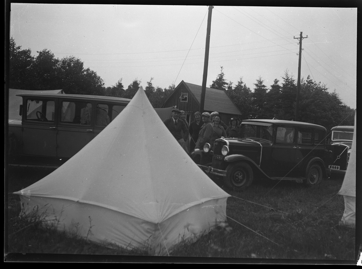 En grupp personer, tält och bilar på en camping.