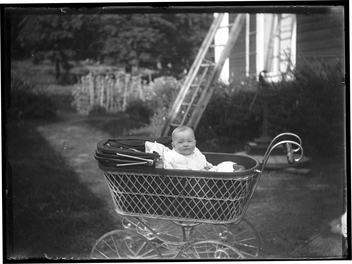 Maja Lindgren i barnvagn i trädgård.
