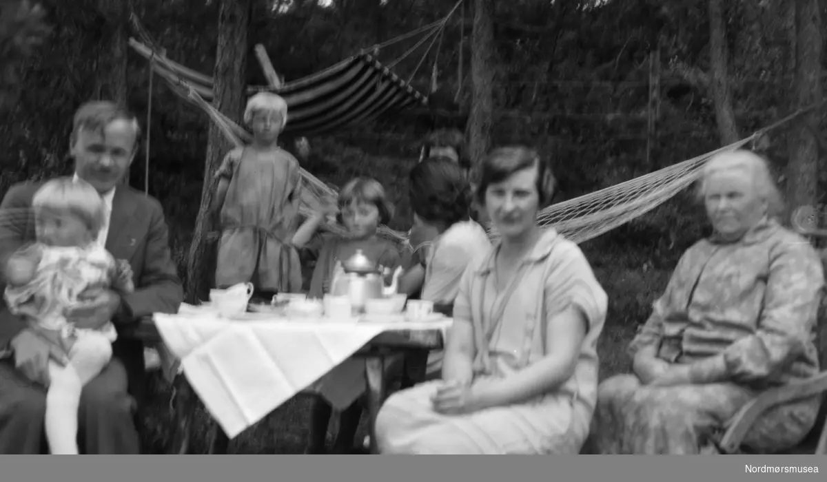Uklart familiefoto ute i en hage. Foto fra en samling av Ida Staurseth Mittet. Fra Nordmøre museums fotosamlinger.
