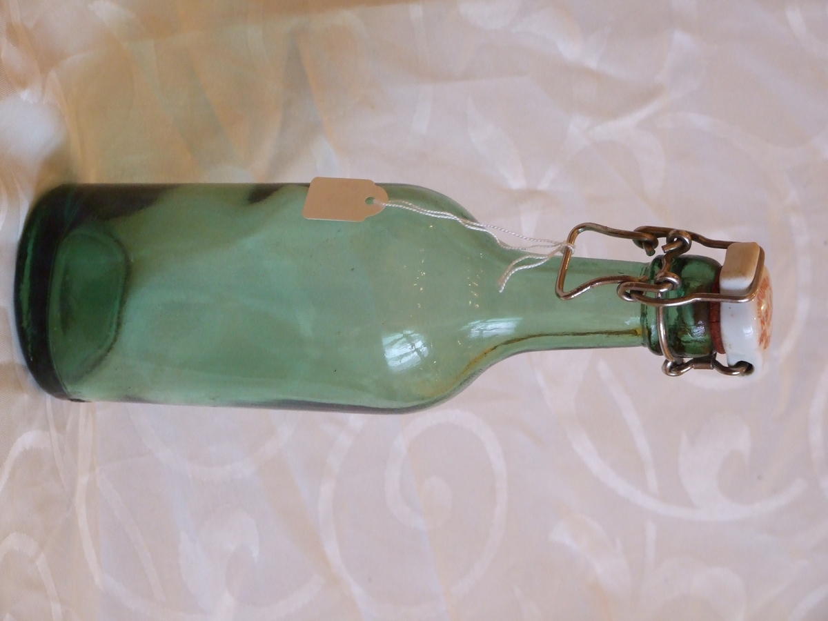Grønn glassflaske med lang tut og patenttropp i keramikk med lukkemekanisme av jern.