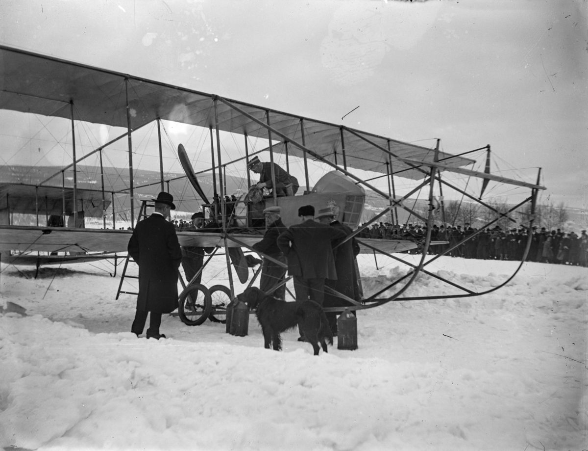 Lillehammer, det første flybesøket i Lillehammer i 1914. Kaptein Einar Sem-Jacobsen står bøyd i flyet. Nærmest flykroppen med sixpence er Roald Amundsen. Flyet er et biplan og skal ta av fra Lysgårdsjordet. Mange tilskuere.