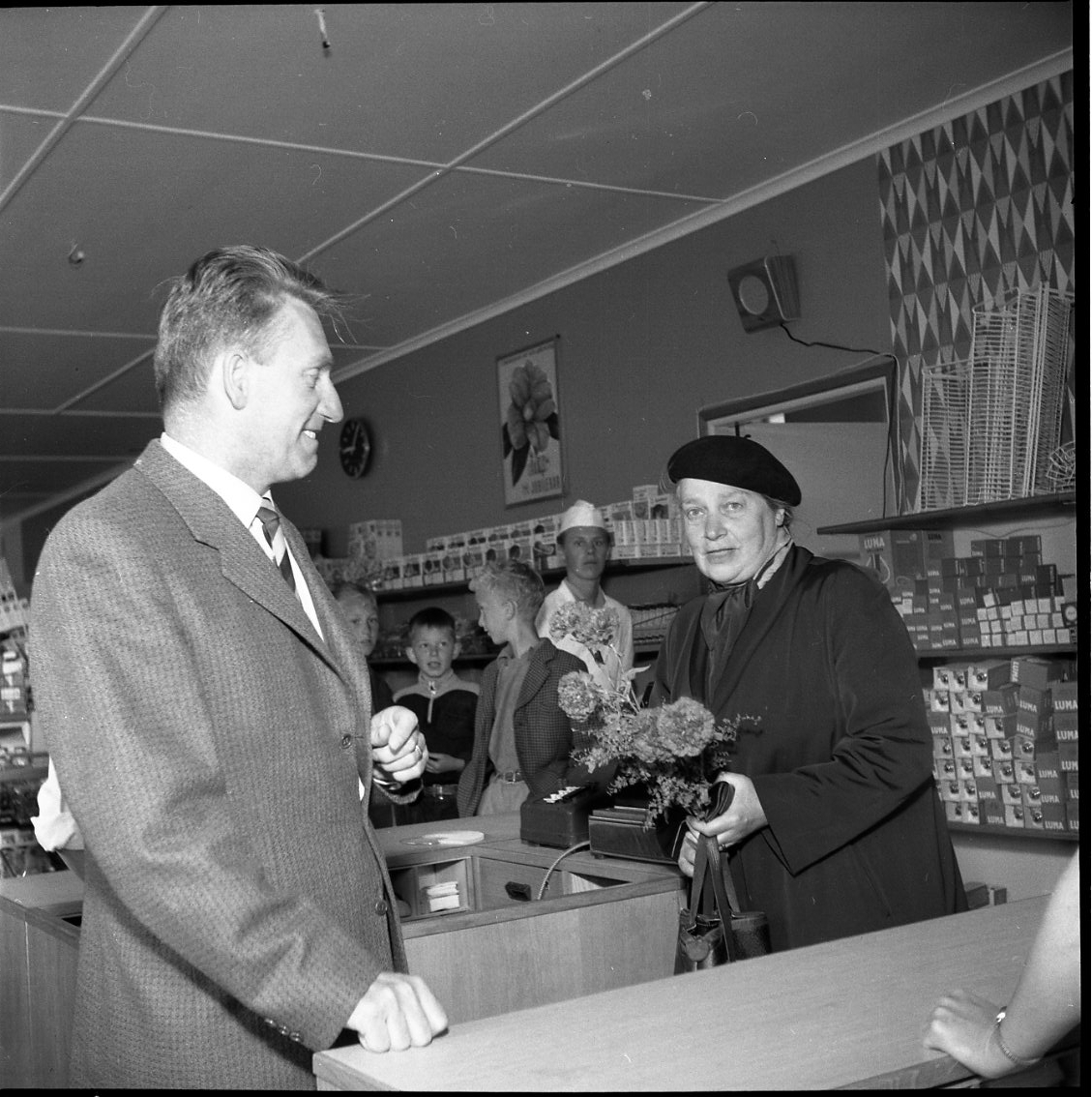 Alfons Holmqvist överlämnar en blomsterbukett till fru Wilma Tholin, den första kunden i Konsum Götas nya snabbköp i Gränna.