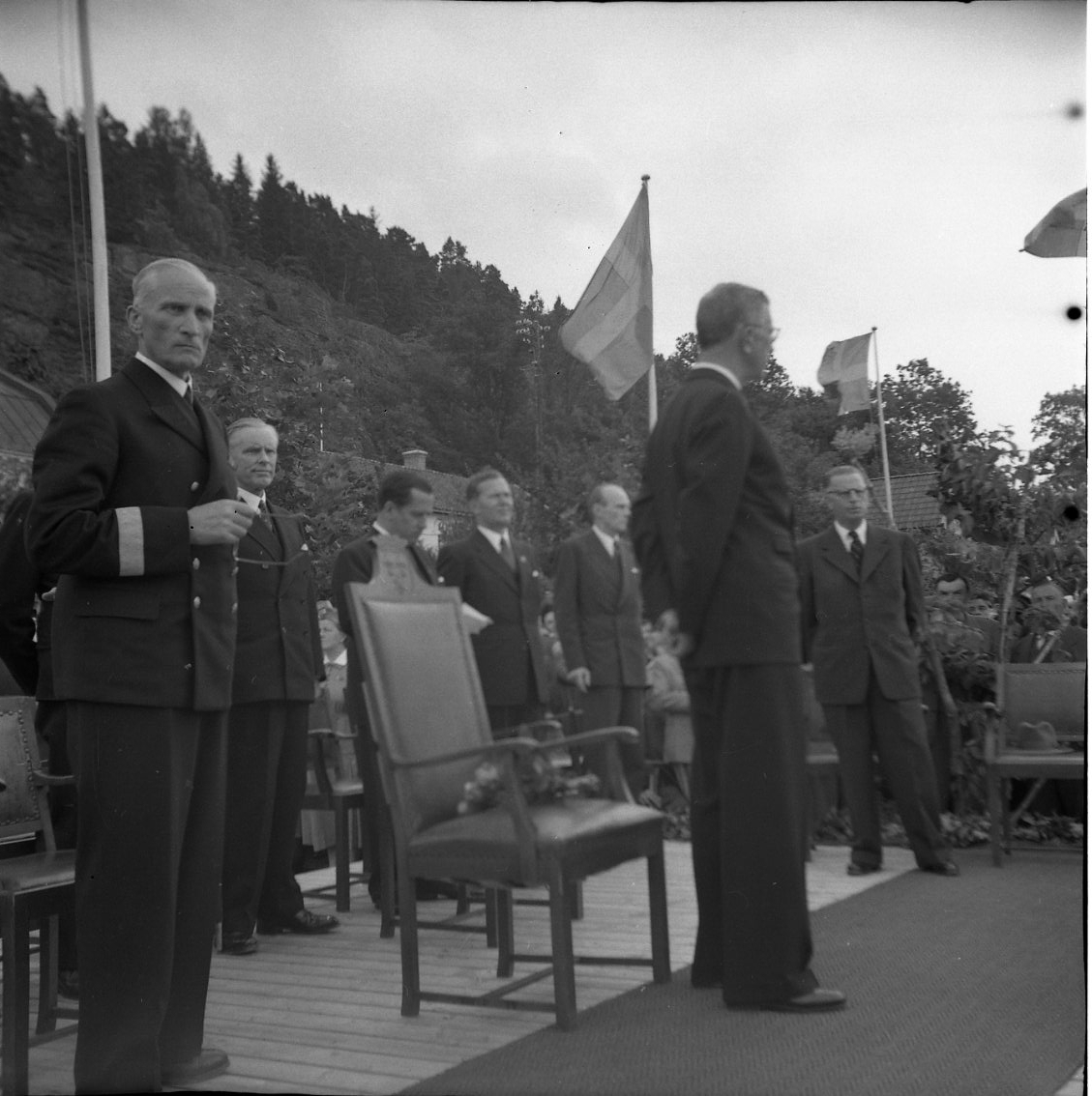 Eriksgata 1954. Kung Gustaf VI Adolf står på en särskilt uppbyggd estrad i Braheparken. Närmast till vänster står landshövding Olle Ekblom och längst bort till höger står  stadsfullmäktige vice ordf Thure Ekwal. I övrigt okända män i kungens följe