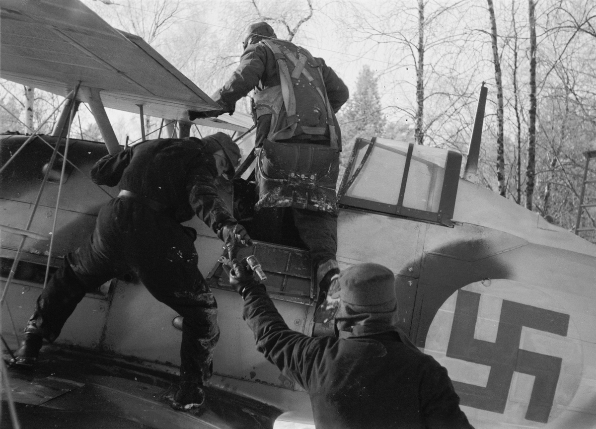 Istigning i flygplan Gloster Gladiator gul F vid F 19, Svenska frivilligkåren i Finland, 20 januari 1940. Flygförare Martin Wennerström kliver i flygplan, flygmekaniker startar flygplanet.