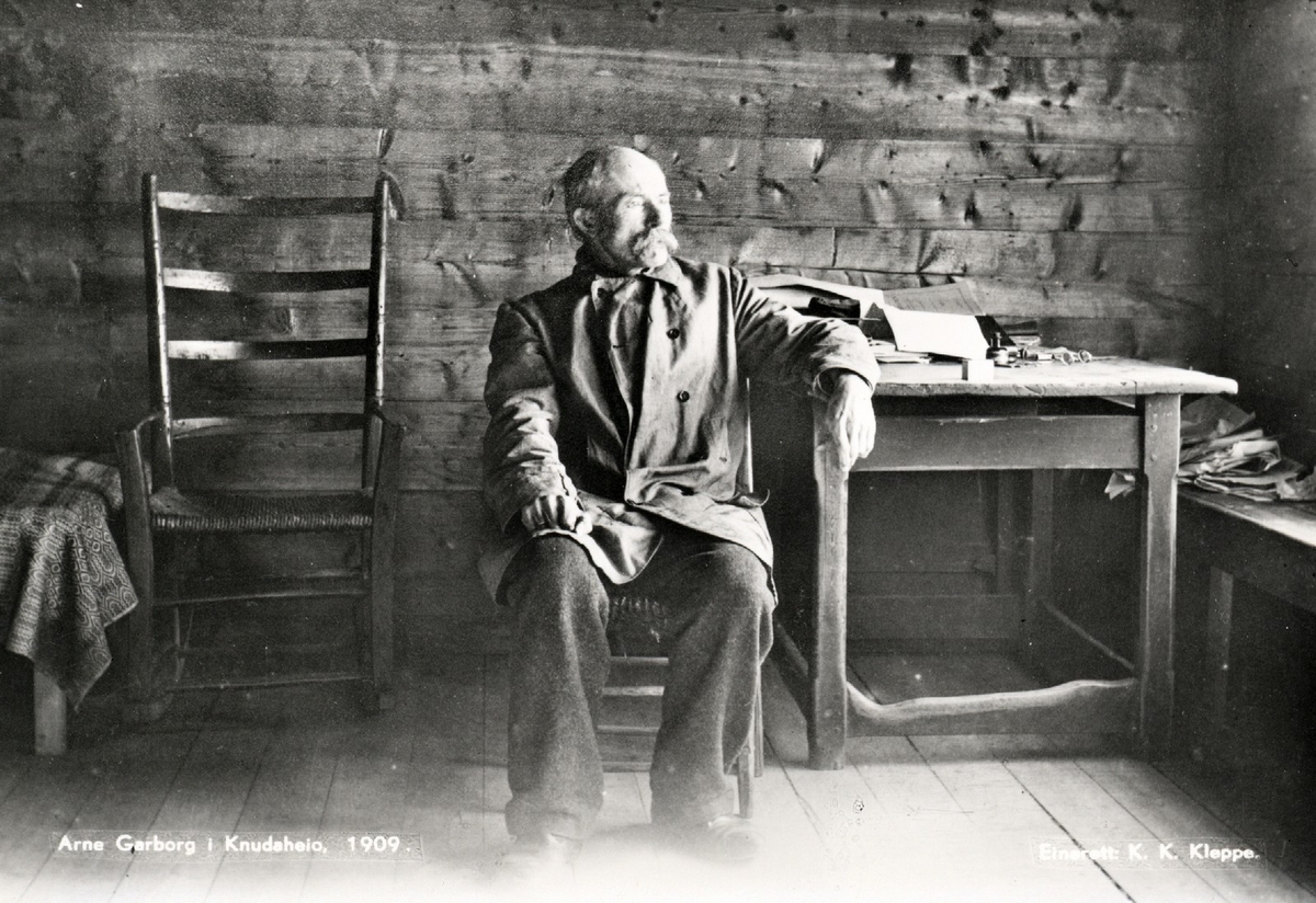 Fotografi av diktaren, målmannen og filosofen Arne Garborg (1851-1924) inne på Knudaheio. Garborg vert rekna blant dei fremste nynorske forfattarane, og han er kjend for verk som romanane "Bondestudentar" (1883), "Trætte Mænd" (1891), "Fred" (1892), og diktsyklusen "Haugtussa" (1895). Garborg var også engasjert i landsmålsrørsla. Han grunnla avisa "Fedraheimen" i 1877, og var med på skipinga av tidsskriftet "Syn og Segn" i 1894 og avisa "Den 17de Mai" i 1904. I 1913 var han medverkande til skipinga av "Det Norske Teatret". Huset Knudaheio i Time på Jæren, vart bygd i 1898 av Garborg, og nytta som feriestad og diktarstove. Fotografen er Karl Korneliusson Kleppe (1877-1959).

Dette er eit digitalt eksemplar av eit foto frå biletarkivet etter "Norsk Allkunnebok". Fonna Forlag gav ut det nynorske leksikonet "Norsk Allkunnebok" mellom 1948 og 1966. Biletarkivet vart utlånt frå Nasjonalbiblioteket til Nynorsk kultursentrum, og kan kopierast og nyttast av sistnemnde etter avtale frå 2004.

Kjelde:
https://www.allkunne.no/framside/biografiar/g/arne-garborg//90/3943/ (Lesedato: 24.03.2020)
https://no.wikipedia.org/wiki/Knudaheio (Lesedato: 24.03.2020)