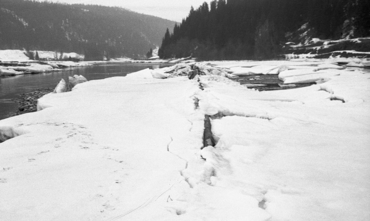 Fra Melvolldammen i den nedre delen av Renaelva i Åmot i Hedmark, fotografert på seinvinteren 1941. Bildet er tatt i motstrøms retning langsetter en såkalt skådam, en skjerm som skulle frastøte tømmeret fra elvebredden og få det til å flyte mot en djupere og mer hurtigstrømmende del av elveløpet. Da dette fotografiet ble tatt var dammen dekt av snø og is, som hadde sprukket der hvor konstruksjonen - antakelig en lav tømmervegg montert på bukker med forankring i en bakenforliggende steinvoll - møtte elva. Fotografiet ble antakelig tatt fordi funksjonærene i Glomma fellesfløtingsforening mente at flytende tømmer, rennende vann, snø og is hadde tæret så hardt på konstruksjonen at den måtte repareres.
