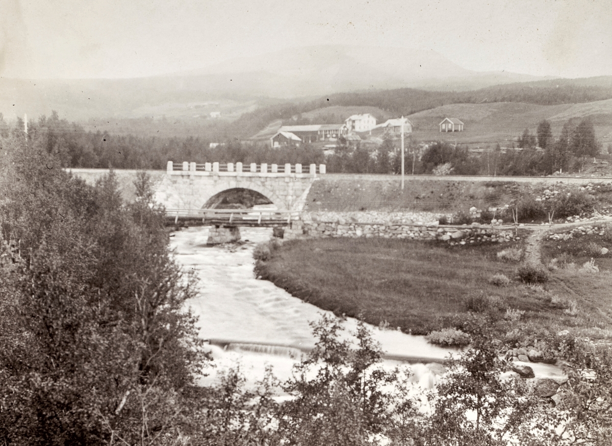 Motiv av gamle Geilo bro sammen med en nyere bro. I bakgrunnen er et større gårdsbruk.