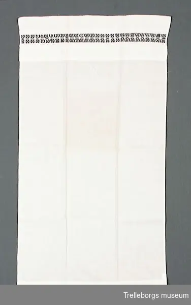 Vitt överlakan till  docksäng. 4 cm från ovankanten är en 2,5 cm bred spets infälld.
Samma spets och märkning som örngott TM.77:409.