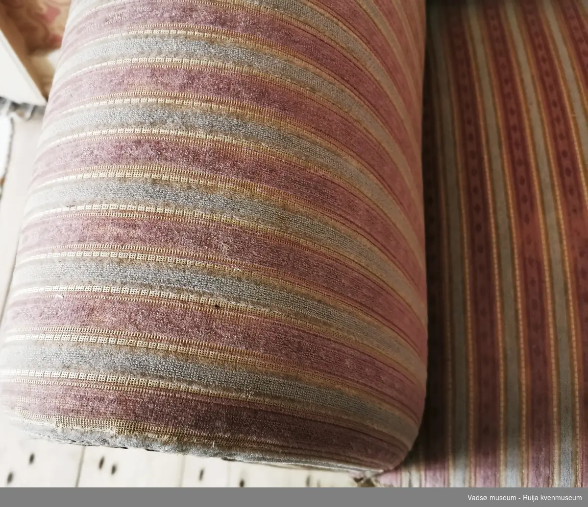 Rektangulær sofa i Biedermeier-stil. S-formet ryggbrett. Glatt, profilert rygglist. S-formede utoversvungne lener og lett utoversvungne bein. Lener, nedre kant av sargen og sofabeina er dekorert med utskåret blad-/knoppedekor. Sofaen er stoppet og er trukket i rosa, hvitstripet stoff.