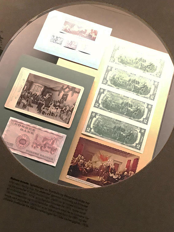 Foto av gjenstander i monter i utstillingen der de to maleriene er motiver på postkort, sedler og frimerker. (Foto/Photo)