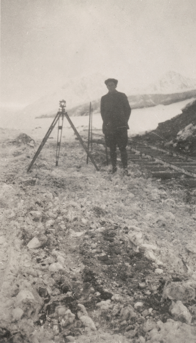En mann står ved ei jernbane med et landmålingsinstrument.