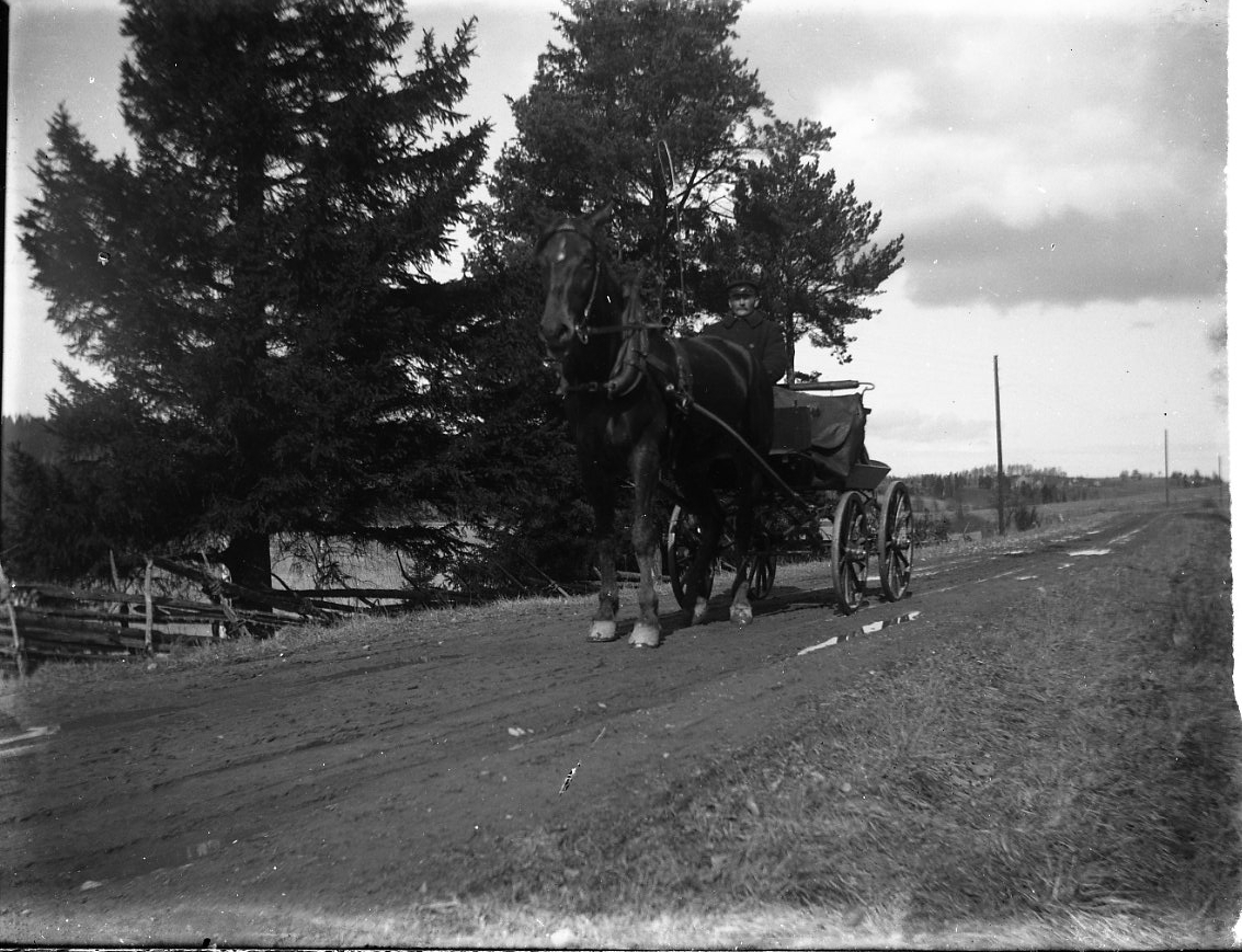 Häst och vagn med okänd kusk på en grusväg.