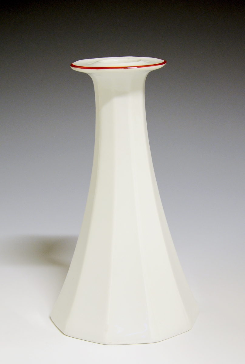 Mangekantet lysestake av porselen med hvit glasur, dekorert med en enkel rød strek langs lysestakens krage.
Modell: Octavia, tegnet av Grete Rønning i 1977
Dekor: Rød strek