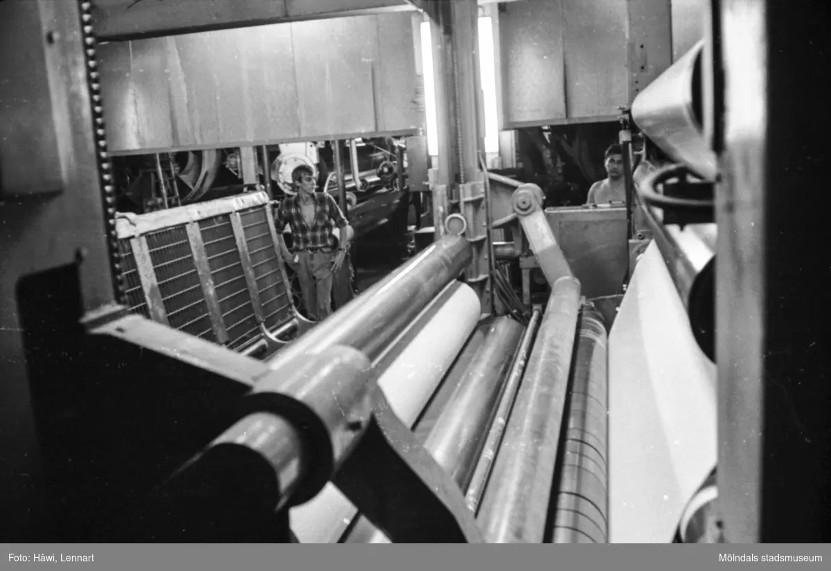 Män i arbete vid rullmaskin 5, byggnad 10. Rullmaskinförare Göran Sjöberg till vänster. Pappersbruket Papyrus i Mölndal, hösten 1970.