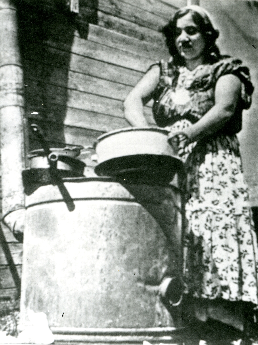 En ung kvinna står framför en yttervägg och diskar. Bildens ursprung är okänt.