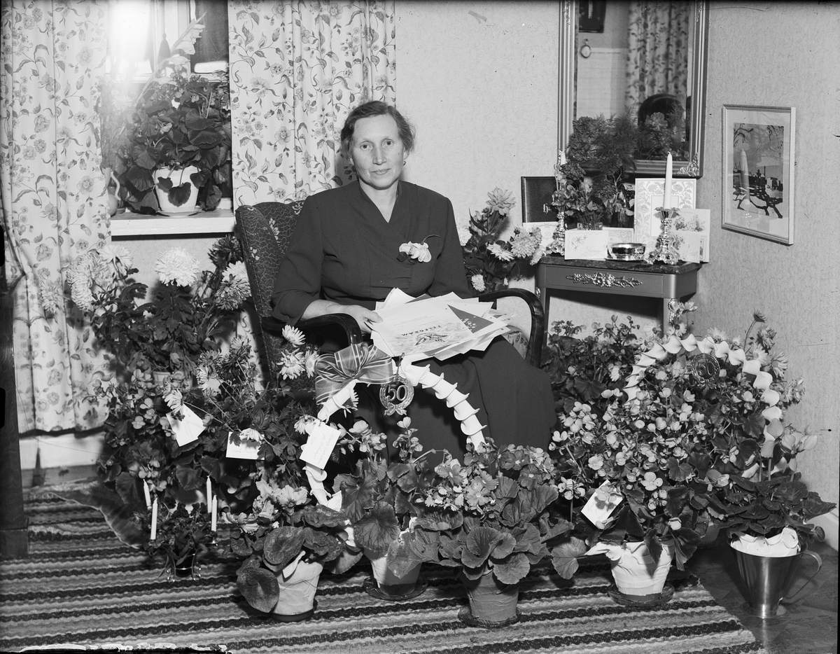 Kvinna i hemmiljö omgiven av blommor firar 50-årsdagen, Östhammar, Uppland