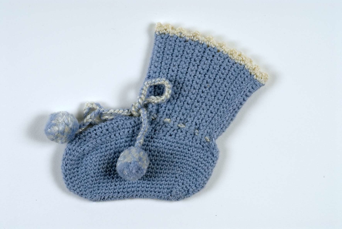 Babysocka av ljusblått virkat garn. Påtad snodd med tofsar, i blått och vitt.