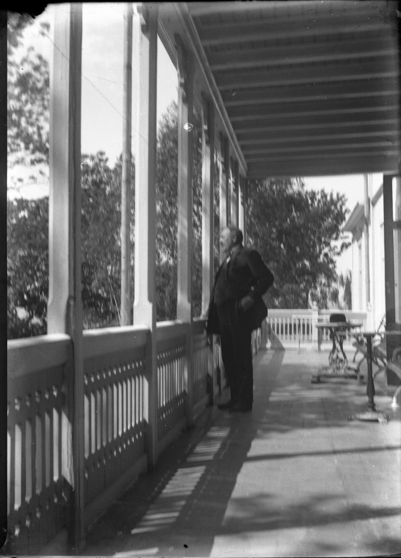 En ensam man står på en stor balkong, han håller en hatt i handen och är vänd utåt. Det är möjligen landshövdning Fredrik Pettersson.