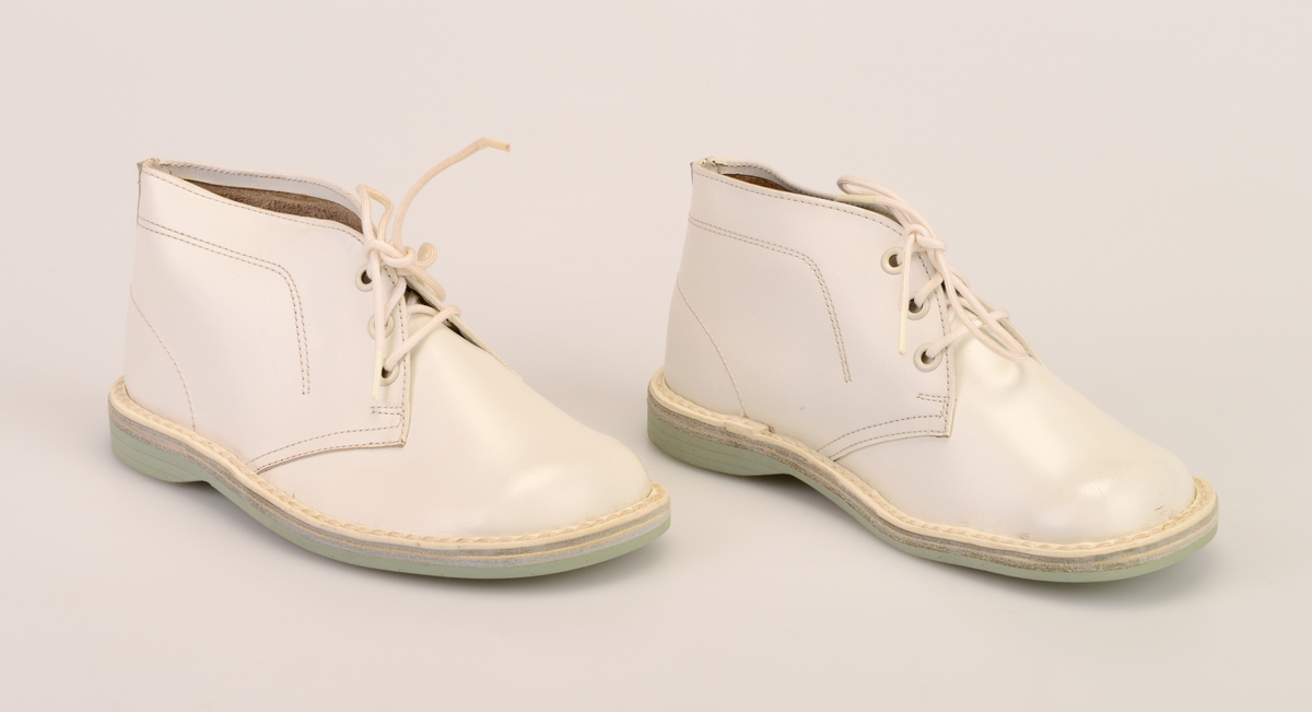 Et par barnesko i størrelse 24 i skoeske med silkepapir. Skoene er i hvitt skinn med såler av lyst grått kunstlær. De er randsydde. I front er det 3 par hull med maljer for snøring. Under snøringen er det en enkel tunge av hvitt skinn. Skoene har hvite, runde skolisser. Det er sømdekor på skoene.  Skoene ligger i en skoeske av papp som er stiftet sammen. På den ene kortsiden er det trykt på fabrikkens navn, varemerke og logo samt artikkelnummer og størrelse. Logoen er en sirkel med en Nord-pil igjennom. Logo og tekst er i rødt med påstemplet artikkelnummer og størrelse i svart. Skoene er ikke brukt.