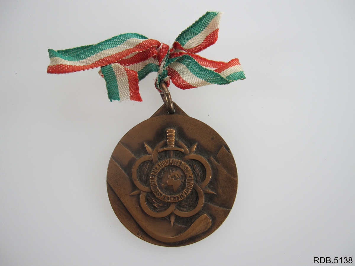 Rund medalje festet til ei sløyfe i rødt, hvitt og grønt. Innskrift på baksiden av medaljen, innskrift og motiv på forsiden av medaljen.