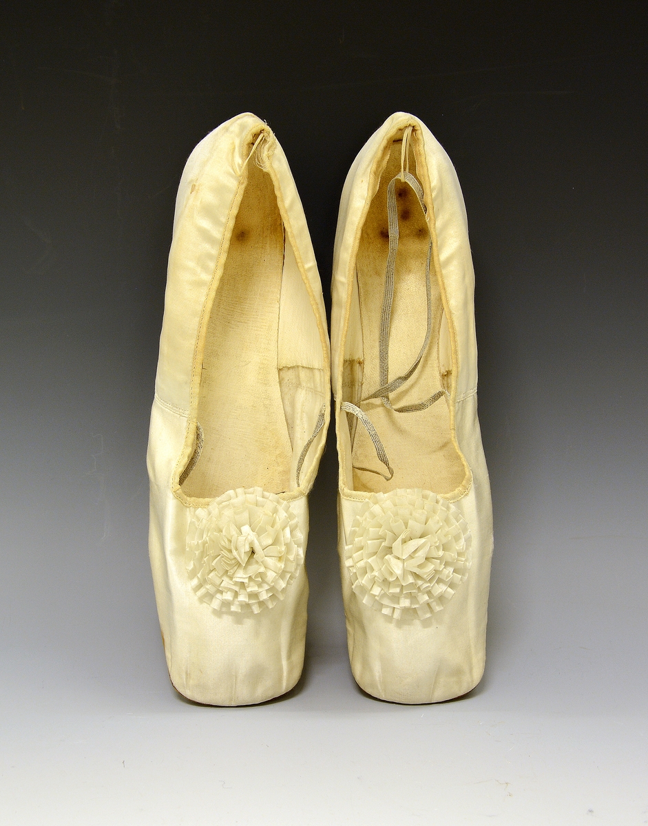 Silkesko. Skoene er formet med bredt tåparti. Sydd av hvit silke og bakre del foret med hvitt semsket skinn. I en hempe bak og på sidene midt på skoen er festet et strikk. Uten fabrikkmerke. Fra protokoll.