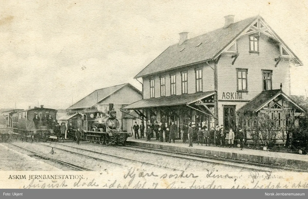Damplokomotiv type 10a med tog på Askim stasjon. Mange reisende på plattformen
