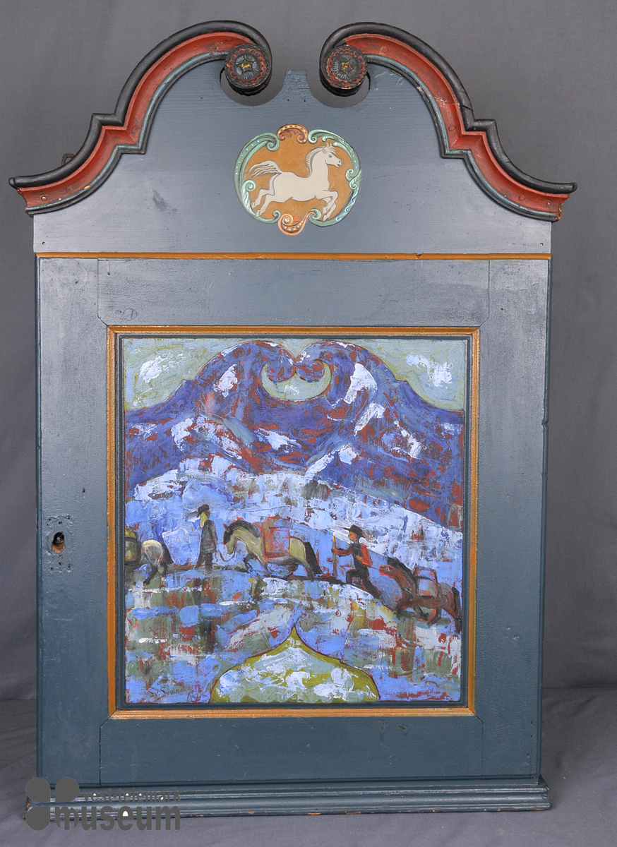 Galopperande hest i grått på brun botn. På spegelen i døra er det måla eit landskap med eit kløvfylgje av tre hestar og to menn.