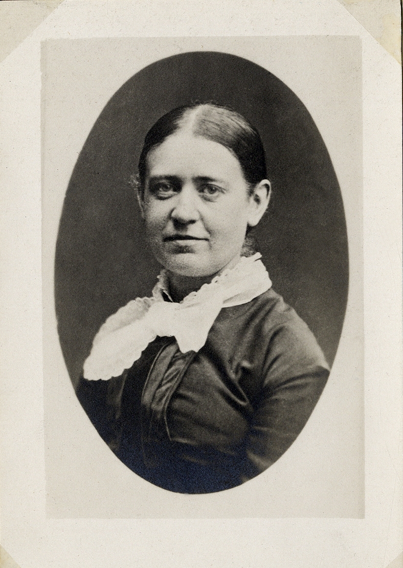Porträttfoto av en kvinna i mörk klänning med vit, spetskantad krage. 
Bröstbild, halvprofil. Ateljéfoto.
