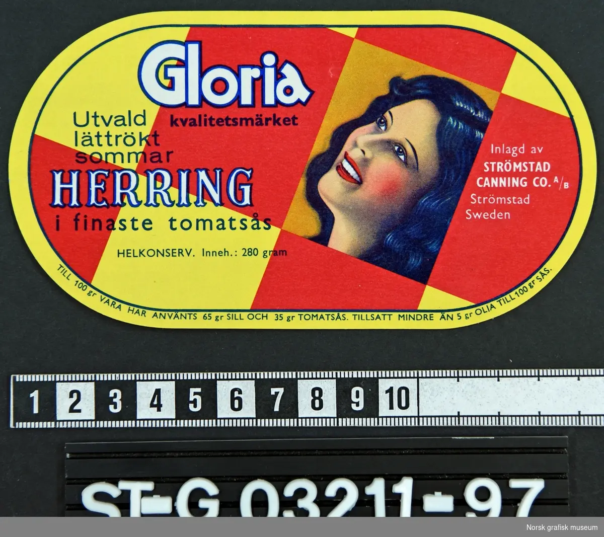 Oval etikett med røde og gule ruter, samt en fremstilling av en mørkhåret kvinne med blikket vendt oppover. 

"Utvald 
lättrökt
sommar 
HERRING
i finaste tomatsås""