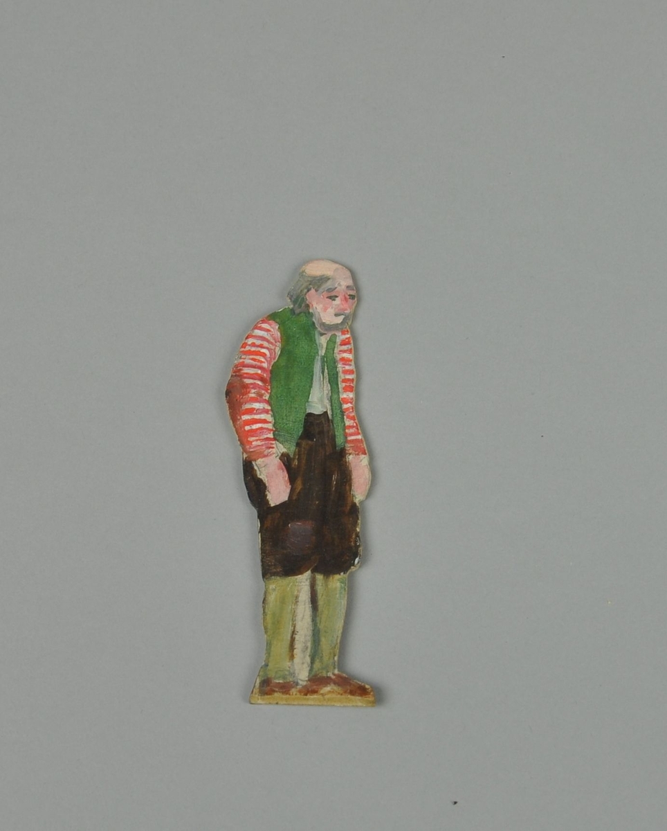 Figur av papp. Figuren forestiller gammel mann, stående i sideprofil. Mannen har nikkers, grønn vest og genser med røde og hvite striper.