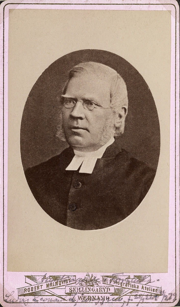 Foto av en äldre man med glasögon och polisonger, klädd i prästrock och prästkrage. 
Bröstbild, halvprofil. Ateljéfoto.