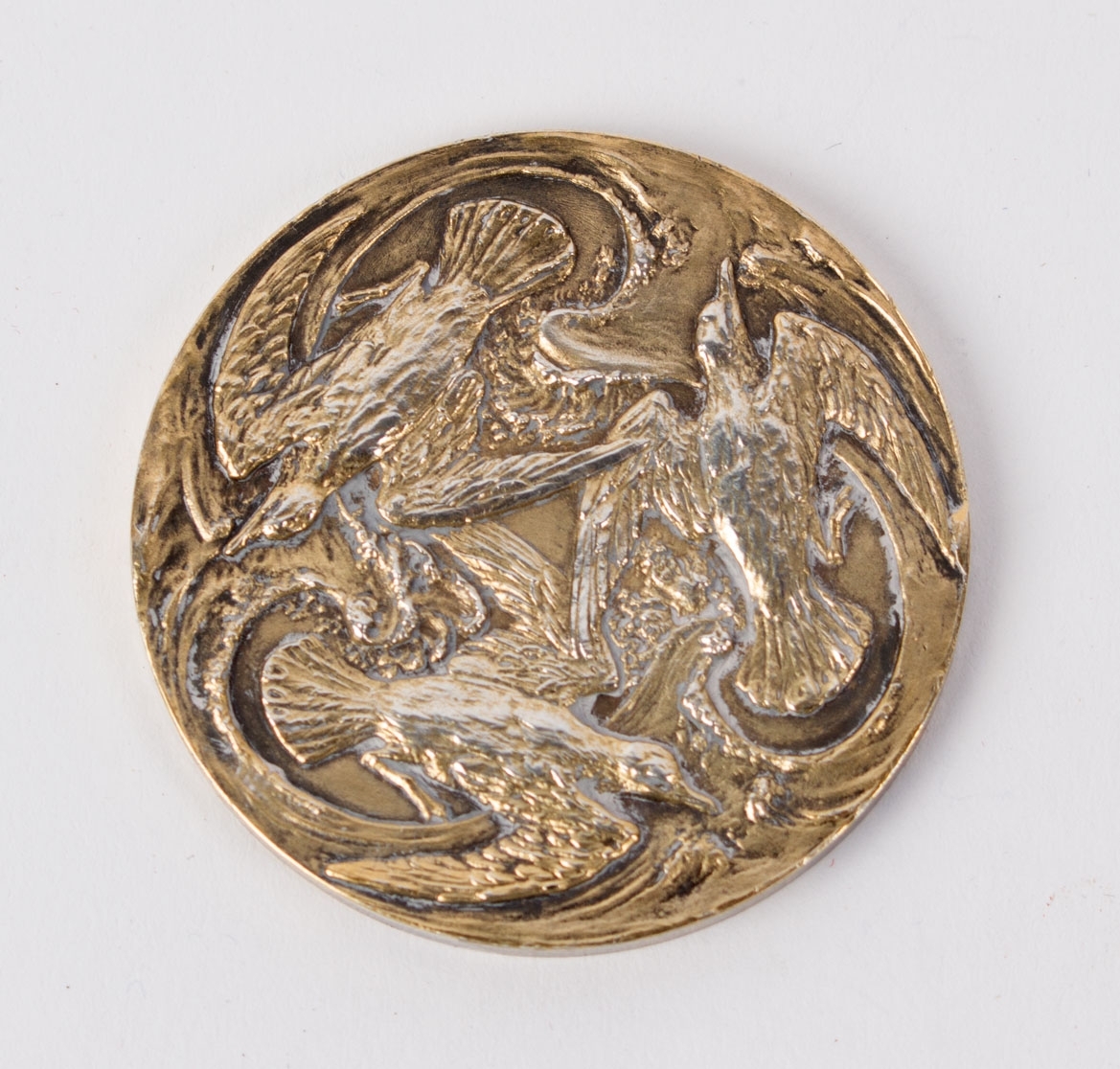 Medalje med motiv av en kvinne/gudinne (overkropp) stående foran et tre. Bakside sees tre fugler. 