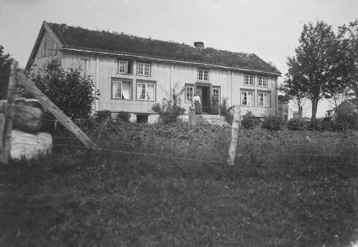 Prospektfotografi av et våningshus på Aukra? Tre kvinner står på trappa foran huset.