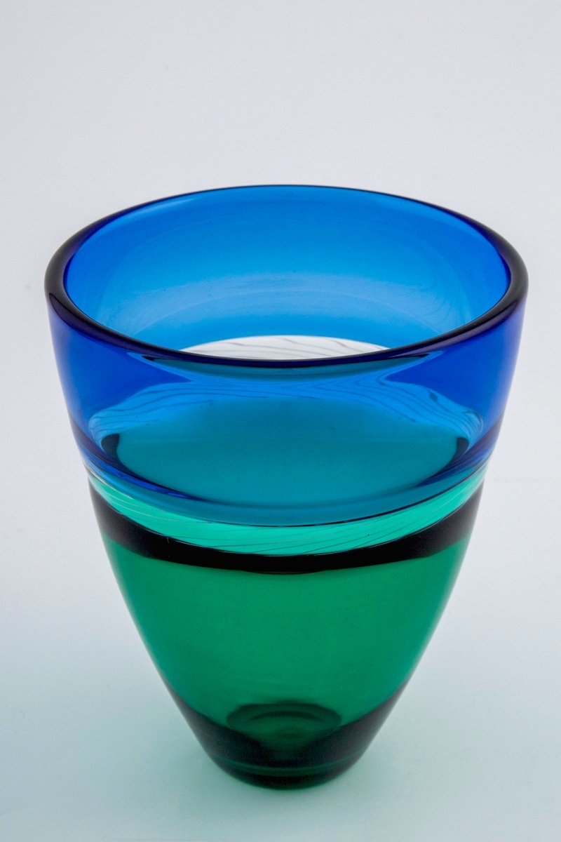 Konisk høyreist vase i polykromt gjennomskinnelig glass. Øverste del er blåfarget, mens nedre del er smaragdgrønn. Overgangen mellom de to delene er markert med et 2 cm bånd i klart glass, dekorert med melkehvite emaljetråder.
