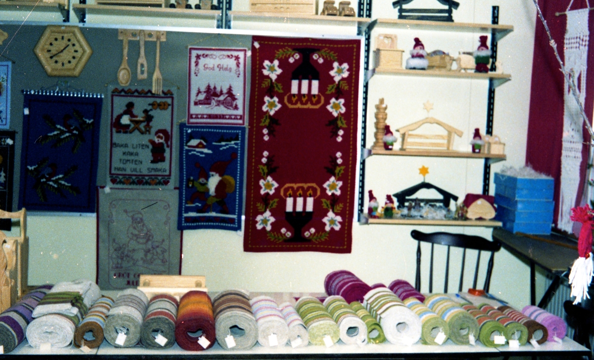 Julförsäljning av hantverk i pensionärernas hobbylokal på Våmmedalsvägen år 1977. I bakgrunden hänger väggbonader, i hyllan står hantverk av trä och på bordet ligger vävda dukar.