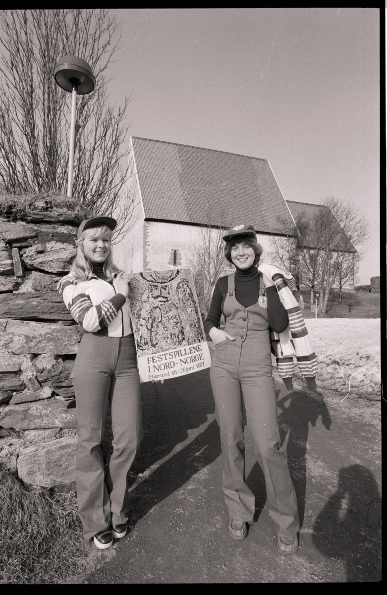 To kvinner viser frem nye drakter og plakat for Festspillene utenfor Trondeneskirka.