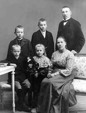 Gruppbild med familjen Stark i Gränna. Mannen Carl står bakom hustrun Ida som sitter i en soffa med blommigt tyg. Fyra barn står (Ernst och Axel) respektive sitter (Nils och Ebba) till vänster.