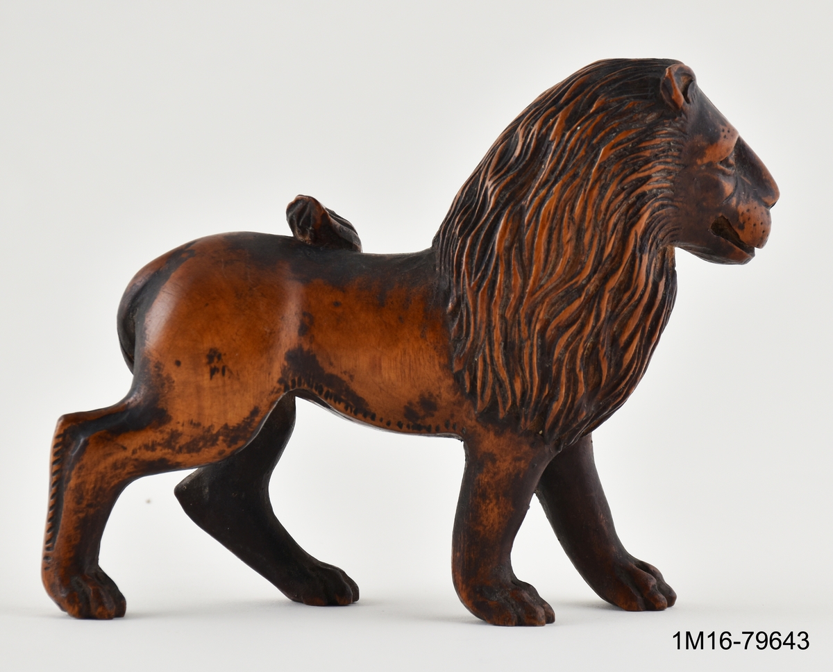 Figurin, lejon, skuret i trä, stående med svansen över ryggen.
