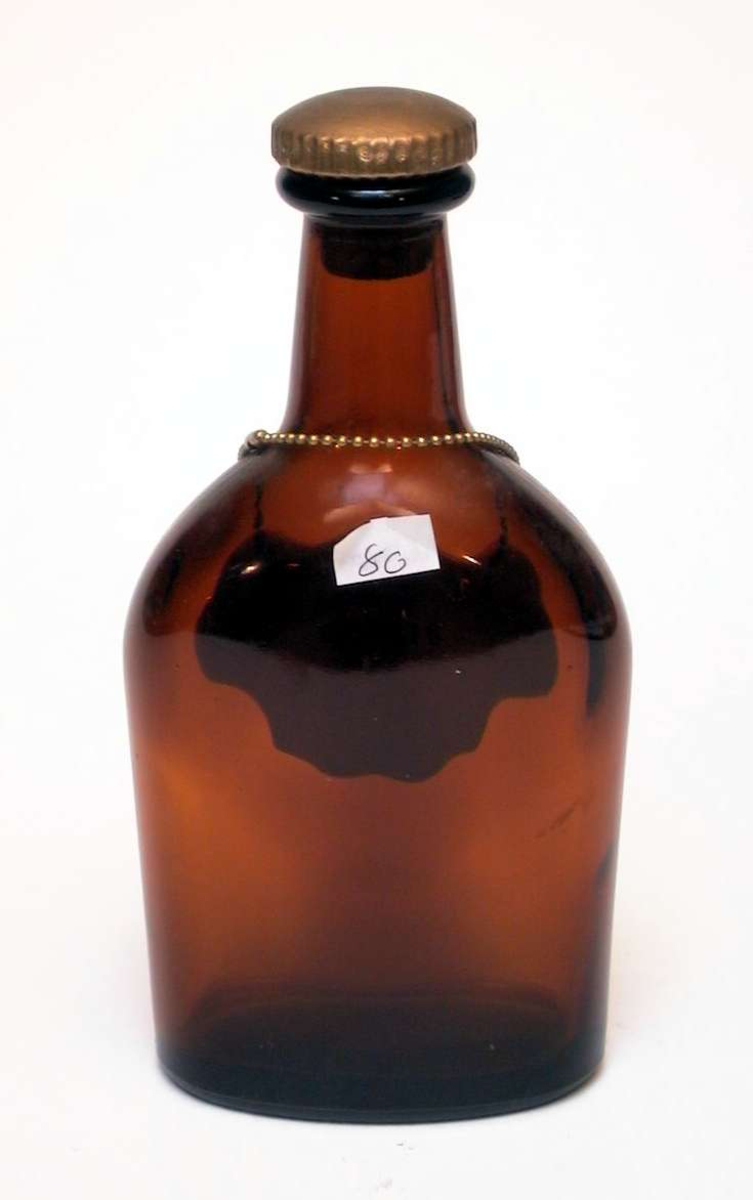Flat brennevinsflaske i brunt glass med kork. Rundt halsen på flasken henger et skilt i lenke. Det er av hvitt glass, dekorert med blomster og er påskrevet 'Whisky'.