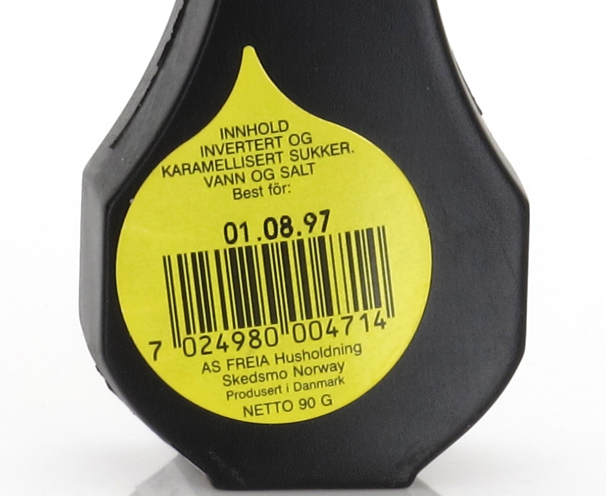 Liten plastflaske med skrukork, flasken er sort, korken gul. 
 Stempel fra  produsent i bunnen. Tilstand god.