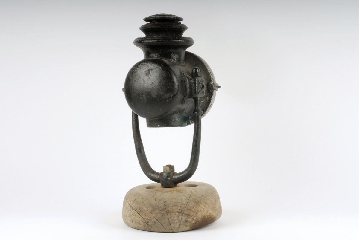 Form: Sylinderformet lykt med rundt glass i fronten.
Stativ av jern satt ned i foten. Oljedrevet til lampe før 1914 i Tyskland