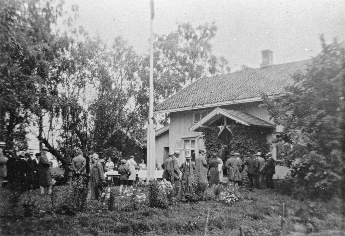 Hos gårdbruker Ruud, Enebakk. Bikongress i Enebakk, Juli 1927. Publikum samlet i hagen. Oppdekket til servering ute. Serveringspersonale i uniform. Sveitserstilhus med flaggstang.
